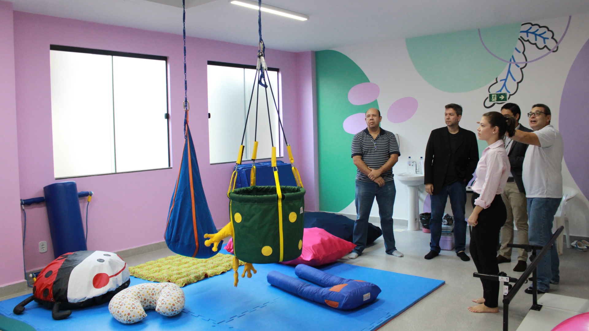 Foto da nova sala de Integração Sensorial do Creap, com brinquedos e materiais lúdicos para as crianças. Quatro pessoas aparecem conversando na imagem. 